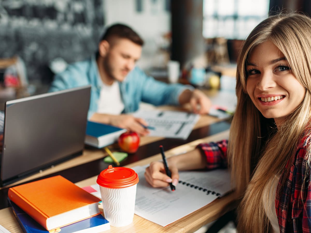 image of a young girl drinking coffee and writing in a notebook with a few other people