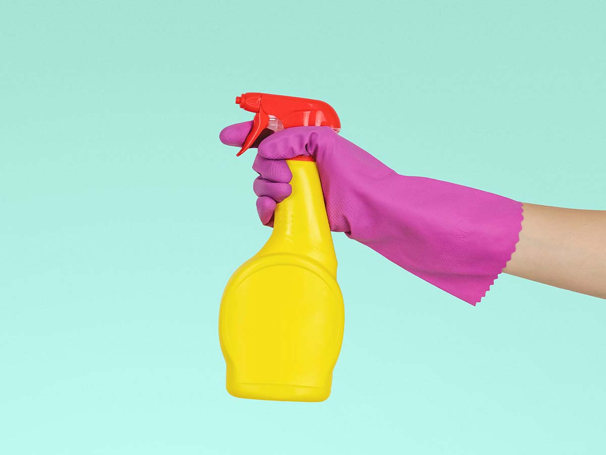 Person wearing a pink rubber gloves aims a yellow and red bottle of cleaning solutions to the left