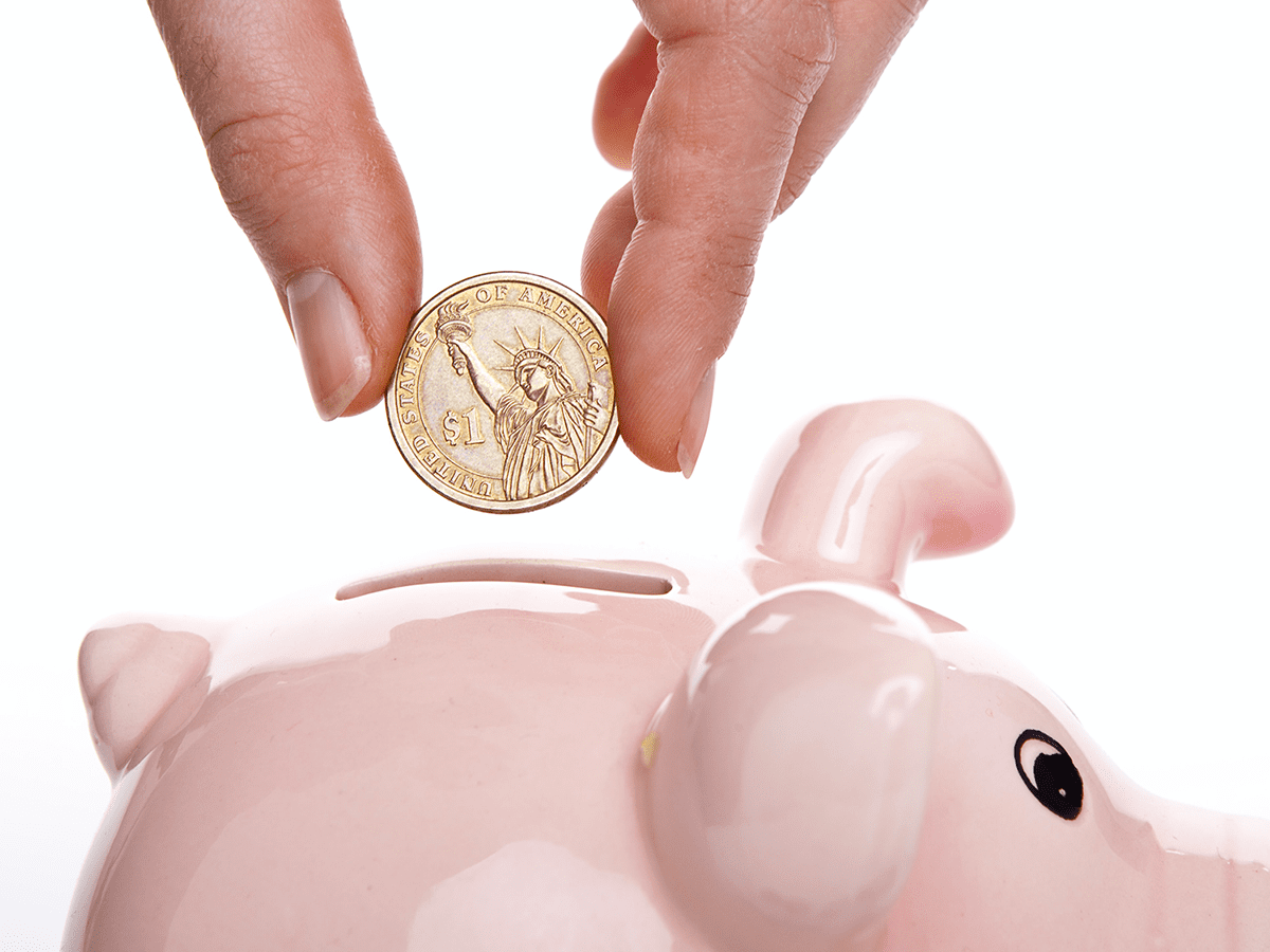 1200x900GMB-3 Person putting a dollar coin into a pink piggy bank