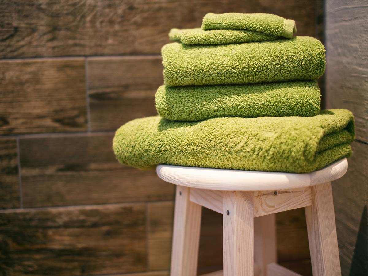 Green towels of various sizes folded and sitting on a wooden stool
