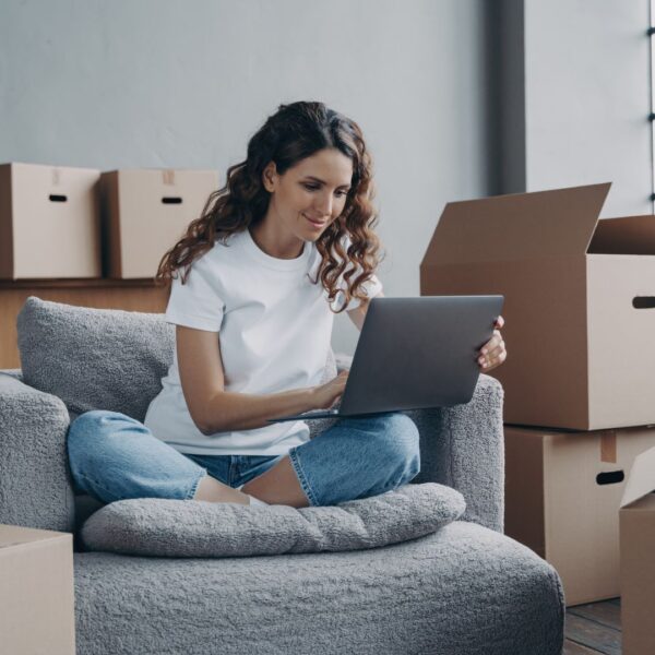 student on couch using laptop to find apartments — moving boxes in background