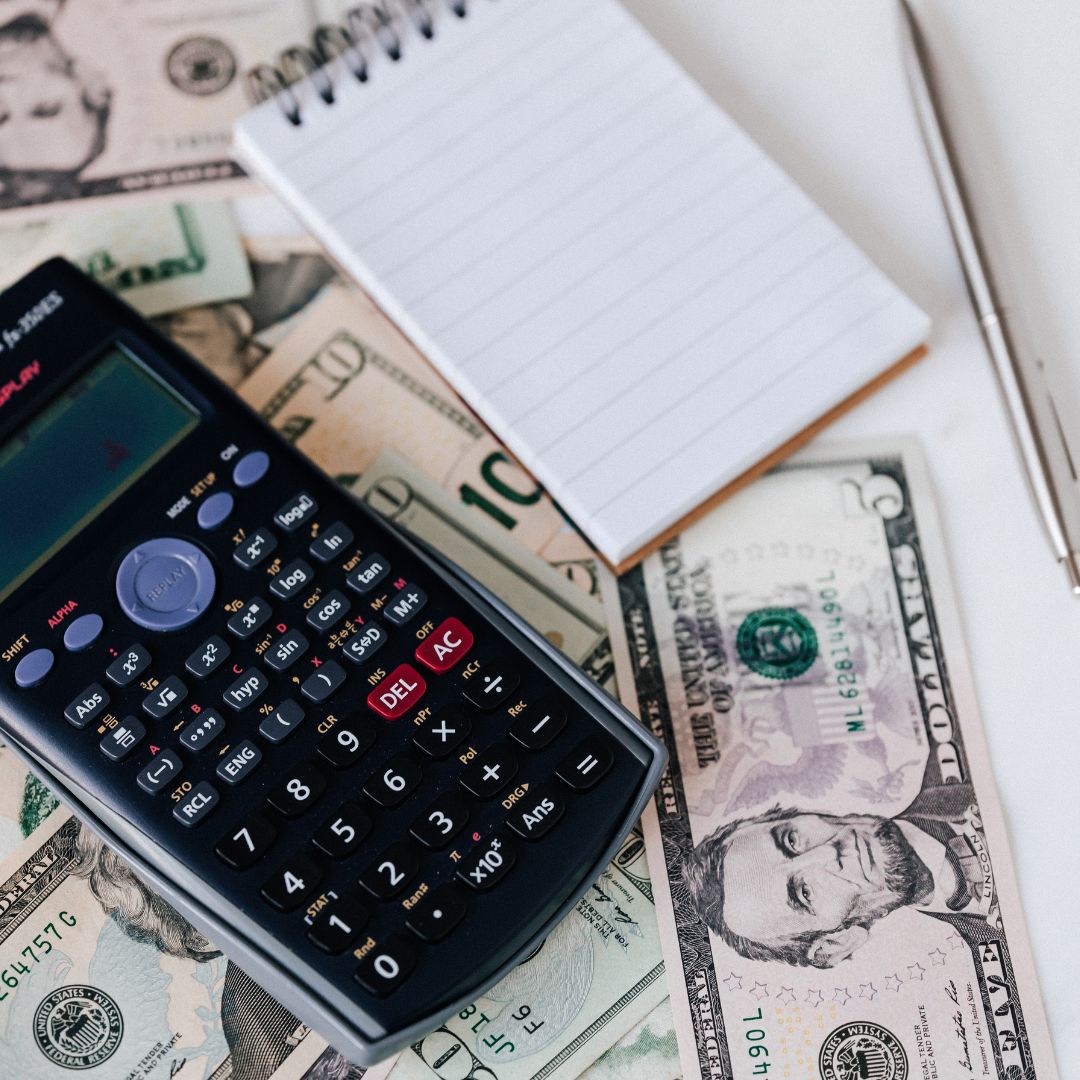 calculator with a notebook and pen on top of money