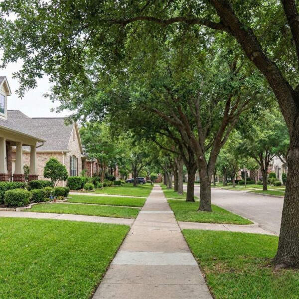 A quiet, tree-lined residential street with sidewalks and well-maintained homes in a College Station neighborhood.